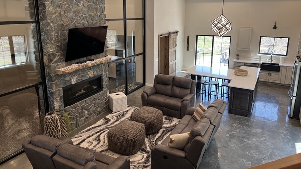 A modern living room with a stone fireplace, a large flat-screen TV, and a cozy seating area. - Secluded, Cozy Shouse near the Lake!  (Roosevelt)