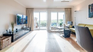 A spacious living room with a large TV, a sofa, a coffee table, and a dining area with a view of the outdoors.