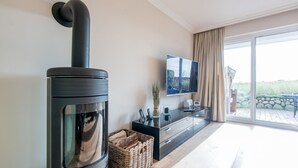 A modern living room with a black wood stove, a flat-screen TV, and a large window with curtains.