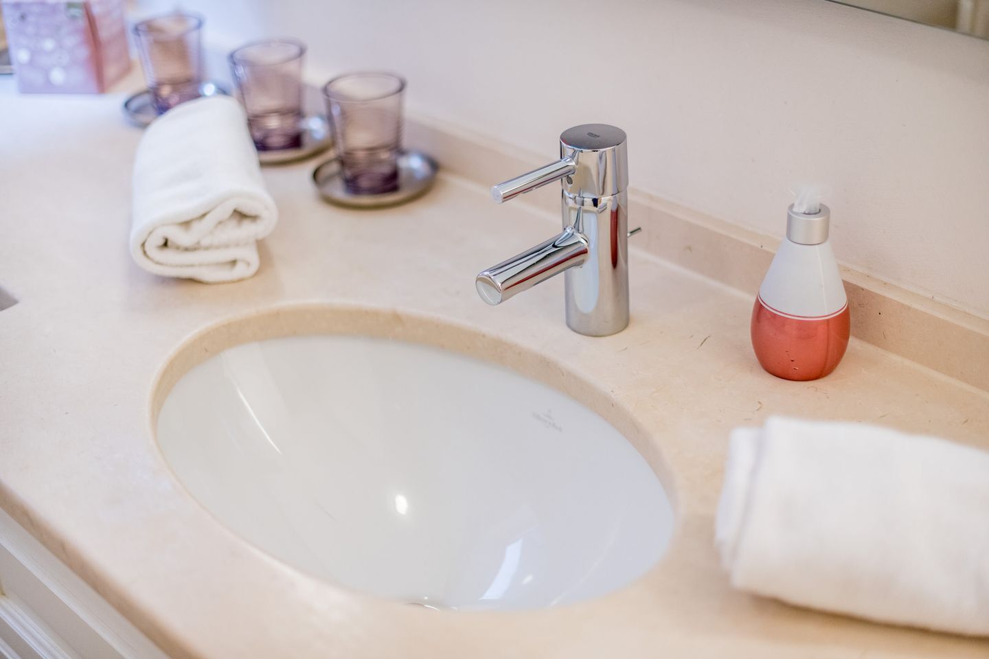 A bathroom sink with a chrome faucet, a tissue dispenser, and two glass candle holders on the countertop.