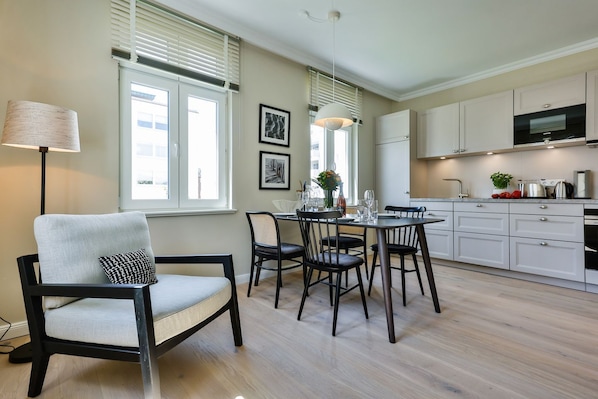 Una cocina moderna con armarios blancos, una zona de comedor con mesa y sillas, y un ventanal con persianas.