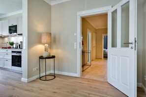 A modern kitchen with white cabinetry, a round table with a lamp, and a hallway leading to a bedroom.