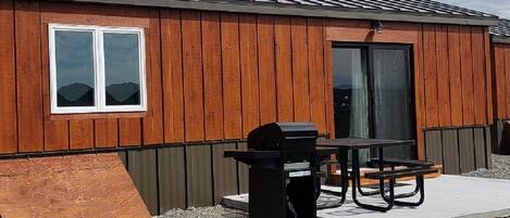 Una cabaña de madera con una parrilla negra, una mesa y un banco.