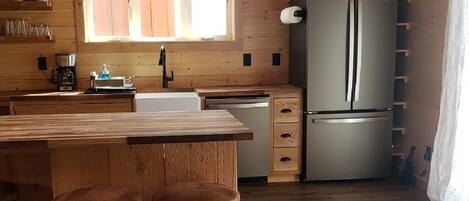 A wooden-paneled kitchen with a large refrigerator, wooden stools, a sink, and a window with blinds.