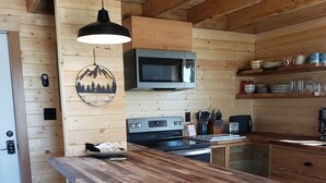 A modern kitchen with a wooden island, bar stools, a microwave, and a stove.