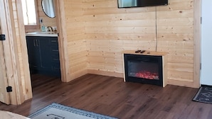 A wooden-paneled room with a fireplace, a mounted TV, and a bathroom with a mirror and sink.