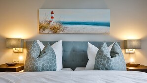 A hotel room with a bed, two nightstands, a headboard, and a painting of a lighthouse on the wall.