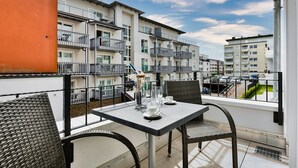 Un balcon avec une table dressée pour deux personnes, des chaises en osier et une vue sur les bâtiments voisins.