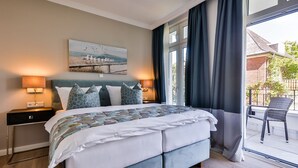 A modern bedroom with a large bed, a headboard with built-in lighting, a nightstand with a lamp, and a view of the outside balcony.