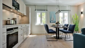 A modern kitchen with built-in appliances, a dining area with a round table and chairs, and large windows with blinds.