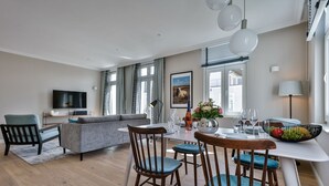 Een moderne woonkamer met een bank, eettafel en stoelen, een flatscreen-televisie en een groot raam met gordijnen.