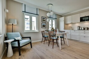 Une cuisine moderne avec des meubles blancs, une table à manger avec des chaises et un luminaire suspendu.