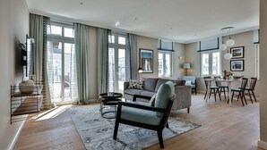 Een ruime woonkamer met een bank, een eethoek met stoelen en een aan de muur bevestigde televisie.