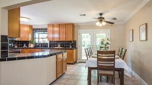 A kitchen with wooden cabinets, a black countertop, and a dining area with a table and chairs. - King Beds! - Clean and Spacious 5 bed 3 bath home (Citrus Heights)
