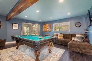 Ein Billardtisch in einem Raum mit blauen Wänden, einem braunen Sofa und einer Wanduhr.
