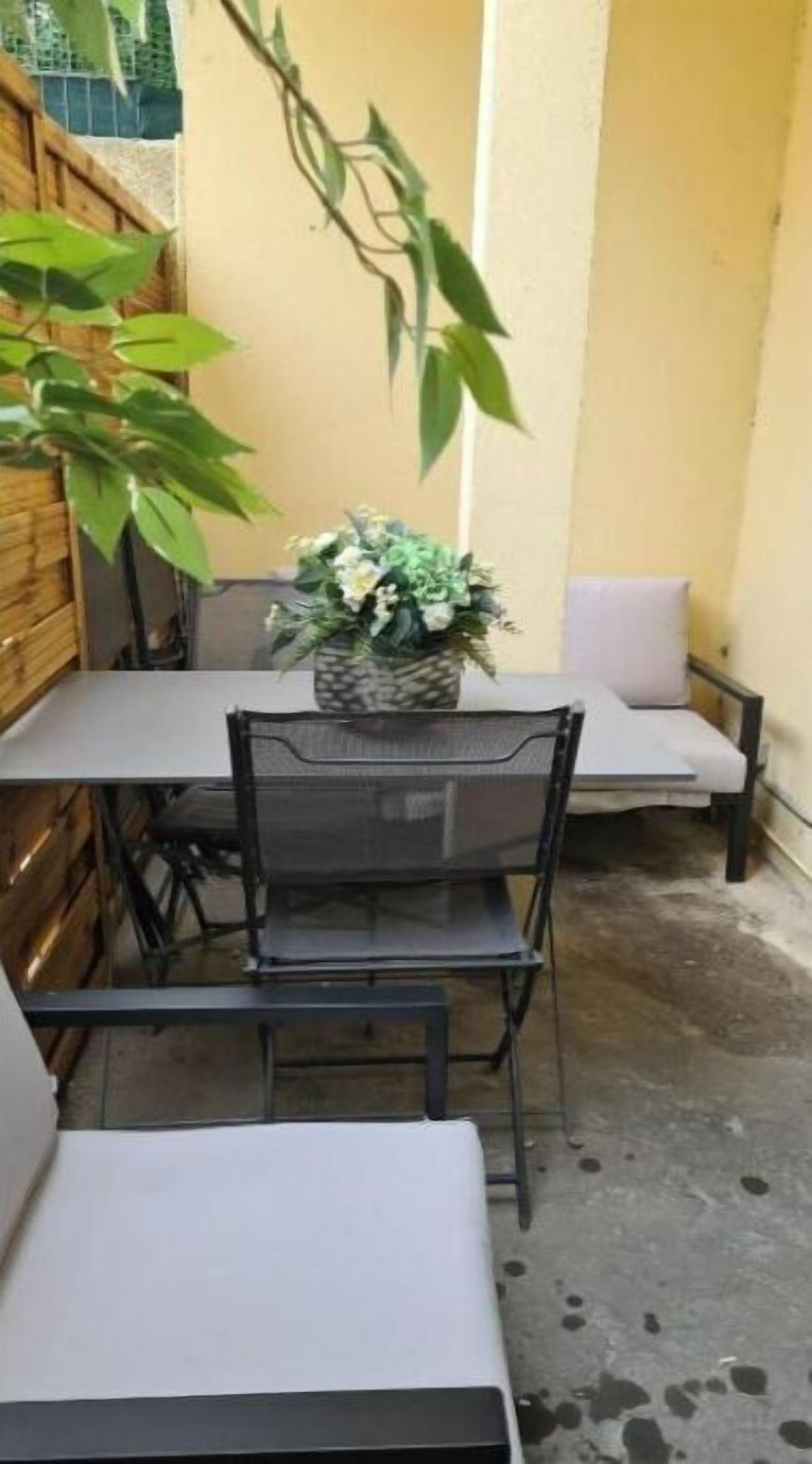 An outdoor patio with a table and chairs, a potted plant, and a concrete floor.