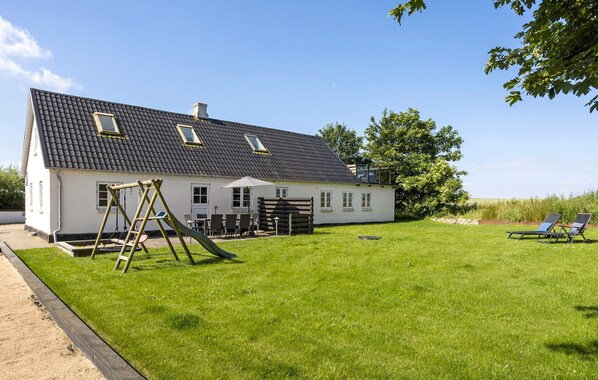 A white house with a dark tiled roof, a swing set, and a small shed.