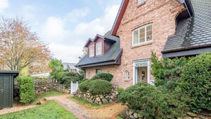 A brick house with a stone wall, a wooden deck, and a well-maintained lawn. - House Sönshörn, Germany (Sylt)