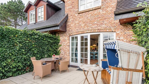 A brick house with a patio, wicker furniture, and a dining area visible through glass doors. - House Sönshörn, Germany (Sylt)