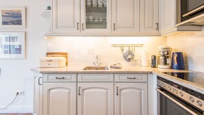 A kitchen with white cabinets, a stainless steel oven, a coffee maker, and a microwave. - House Sönshörn, Germany (Sylt)
