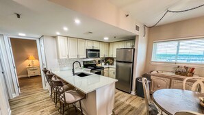 Een moderne keuken met een centraal eiland, roestvrijstalen apparatuur en een eethoek met een tafel en stoelen.