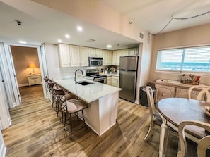 A modern kitchen with a central island, bar stools, a dining table, and a refrigerator.