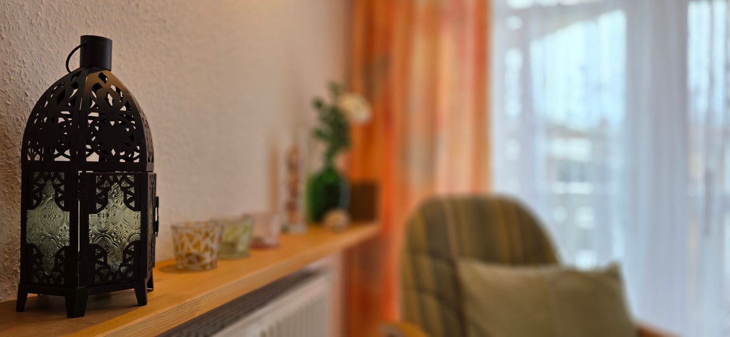 A room with a decorative lantern on a shelf, a chair, and a window with curtains.