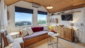 Une pièce chaleureuse avec un plafond en bois, un canapé agrémenté de coussins, une petite table, un téléviseur fixé au mur et une fenêtre donnant sur des immeubles.