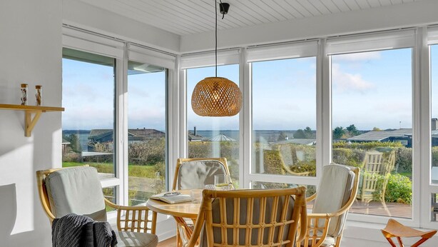 A dining area with wicker chairs and a round table, large windows offering a view of the countryside. - Cozy home in Hurup Thy with WiFi (Hurup Thy)