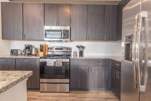 Une cuisine moderne avec des meubles en bois foncé, des appareils électroménagers en acier inoxydable et un plan de travail en granit.