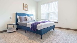 Een slaapkamer met een bed, een nachtkastje, een raam met zonwering en een aan de muur hangend schilderij.