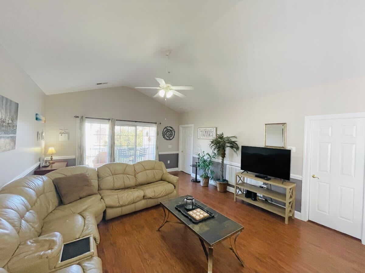 A living room with a sectional sofa, a coffee table, a TV on a stand, and a ceiling fan.