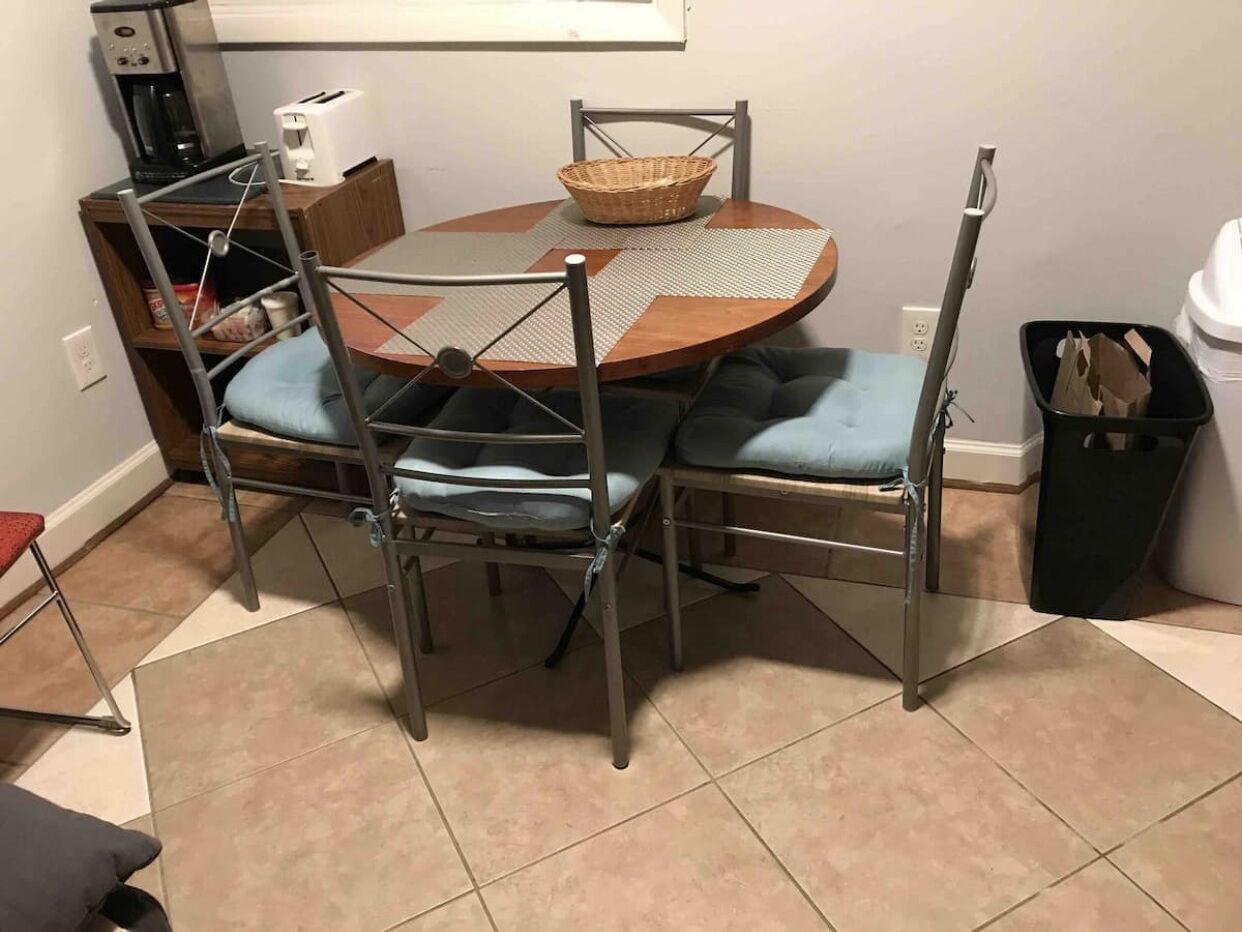 Un coin repas comprenant une table ronde, quatre chaises, une machine à café, un grille-pain et une poubelle.