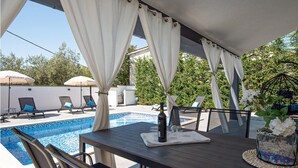 An outdoor pool area with lounge chairs, a table with a bottle and glasses, and white curtains. - Amazing home in Galizana (Galizana)