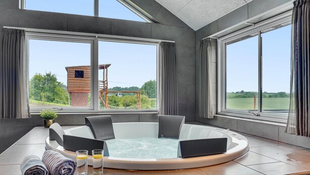 A modern bathroom with a freestanding bathtub, large windows, and a view of a wooden structure outside.