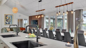 A modern kitchen with a large island, black faucets, and a dining area with a long table and chairs.