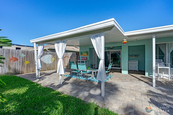 A covered patio area with a table and chairs, a wooden fence, and a sign that reads "Beach".