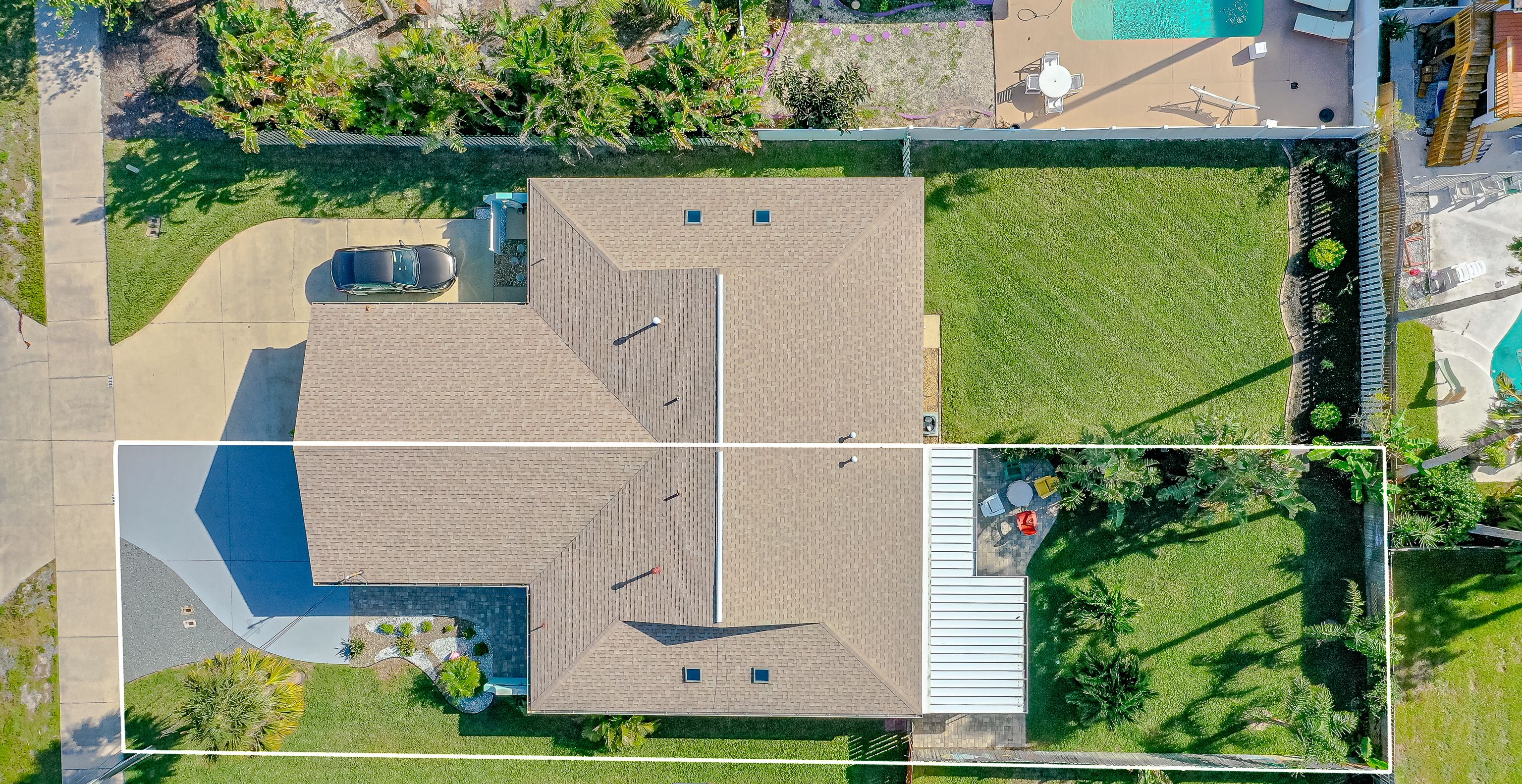 An aerial view of a residential property with a large lawn, a swimming pool, and a patio area with outdoor furniture.