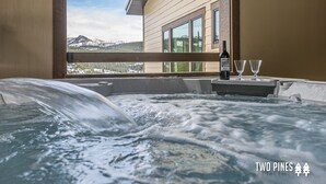 A hot tub with a mountain view, a bottle of wine, and two glasses on a table. - Steps to the Gondola | Ski-In/Ski-Out Luxury Penthouse (Big Sky)