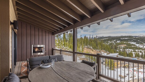 A covered outdoor seating area with a fireplace, a dining table, and a view of a snowy landscape. - Steps to the Gondola | Ski-In/Ski-Out Luxury Penthouse (Big Sky)