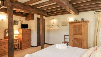 A bedroom with a wooden ceiling, a bed with white bedding, a wooden wardrobe, a desk with a lamp, and a television.
