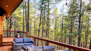 A wooden deck with wicker furniture and a railing overlooking a forest.