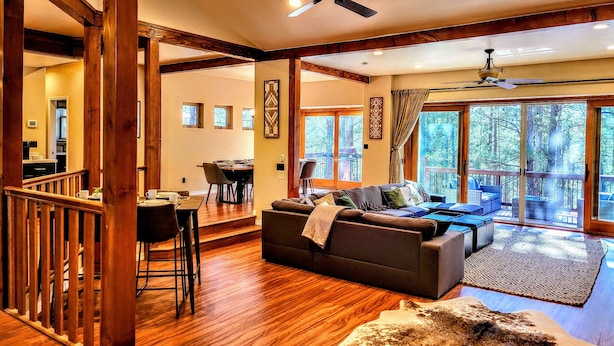 A spacious living area with a wooden floor, a sofa set, a dining table, and a large window offering a view of the outdoors.
