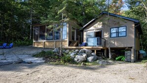 A two-story cabin with a deck, large windows, and a stone foundation.