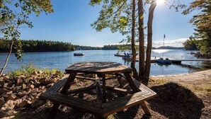 A wooden picnic table by a lake with boats and trees in the background.