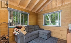Una cabaña acogedora con un sofá seccional gris, ventanas amplias y detalles de madera.