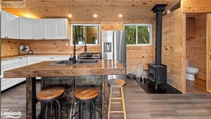 A modern kitchen with wooden cabinets, a central island with stools, a built-in stove, and a large window.