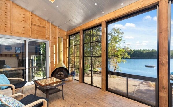 Enjoy a warm atmosphere with a view of the lake from this room, featuring a stove and comfortable seating.