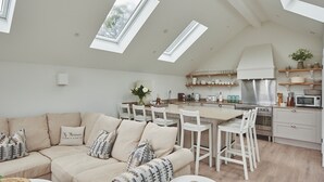 A modern kitchen with skylights, a dining area with white furniture, and a cozy living room with a beige sofa. - Ty Florence - Luxury Cottages (Swansea)