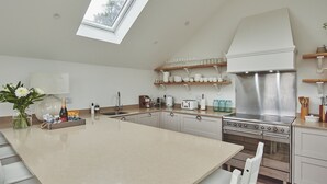 A modern kitchen with a skylight, stainless steel appliances, and white cabinetry. - Ty Florence - Luxury Cottages (Swansea)